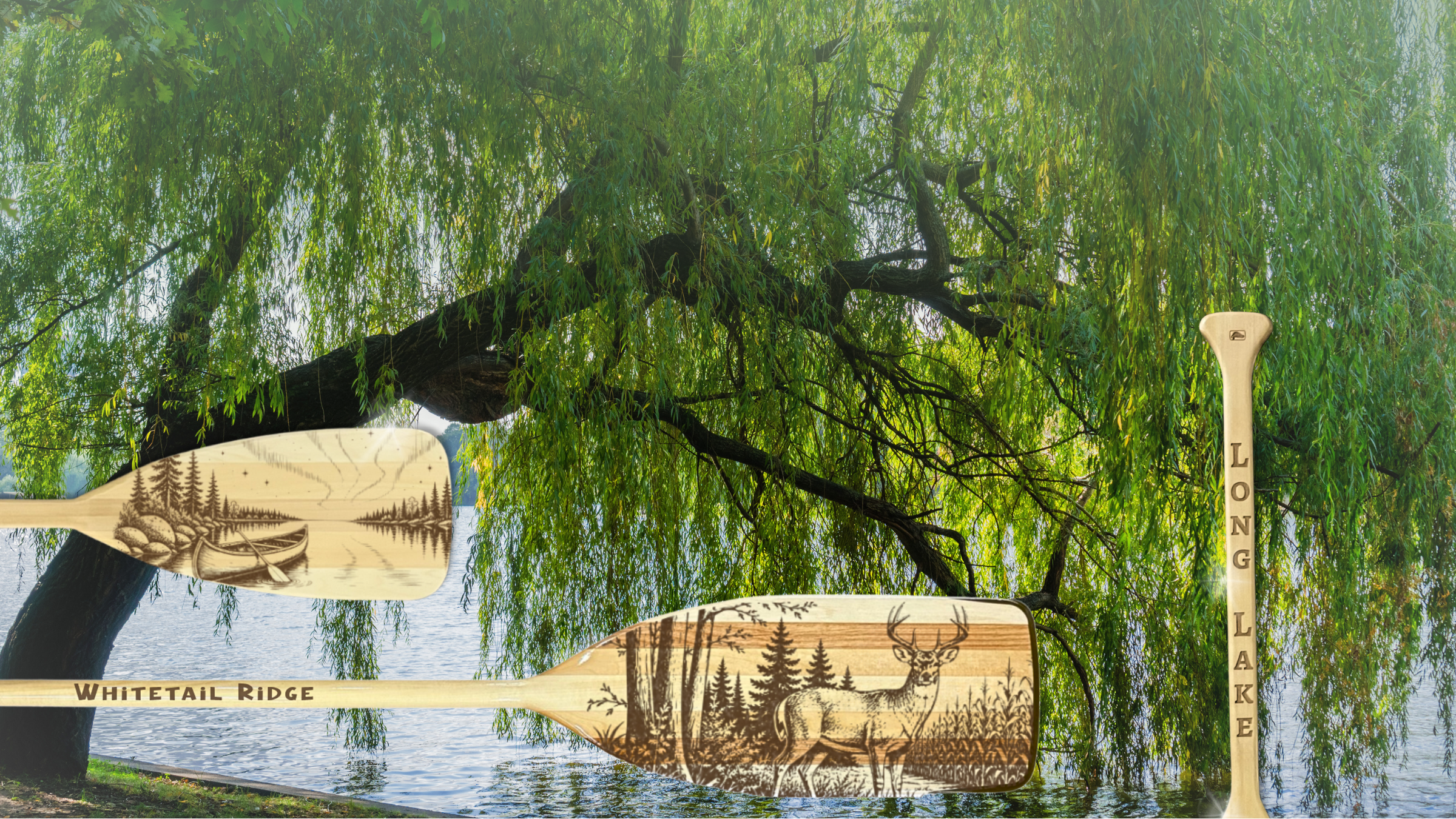 Two carved wooden oars with natural wood grain and engraved wildlife designs, displayed against a background of green weeping willow trees and water. One paddle is labeled 'Whitetail Ridge' and the other vertical paddle shows 'LONG LAKE'.